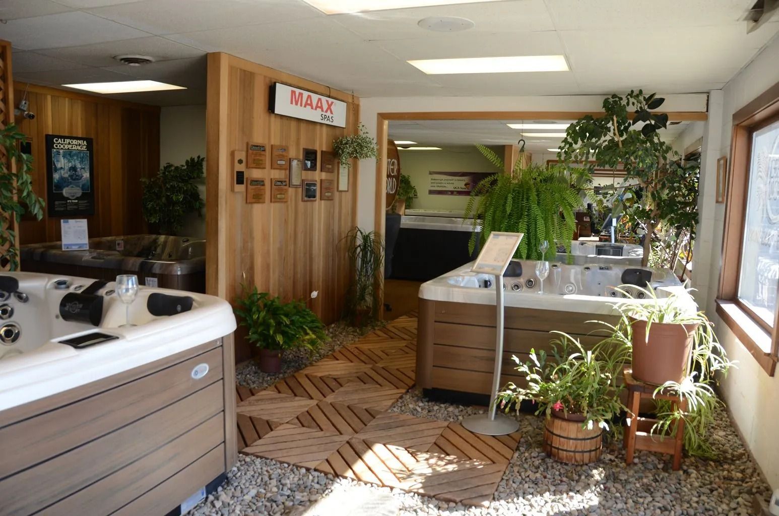 Hot tub showroom with display models surrounded by plants and wood paneling.