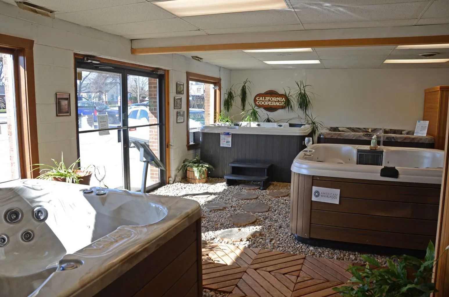 Interior of a hot tub showroom with multiple hot tubs, wood floors, and windows.