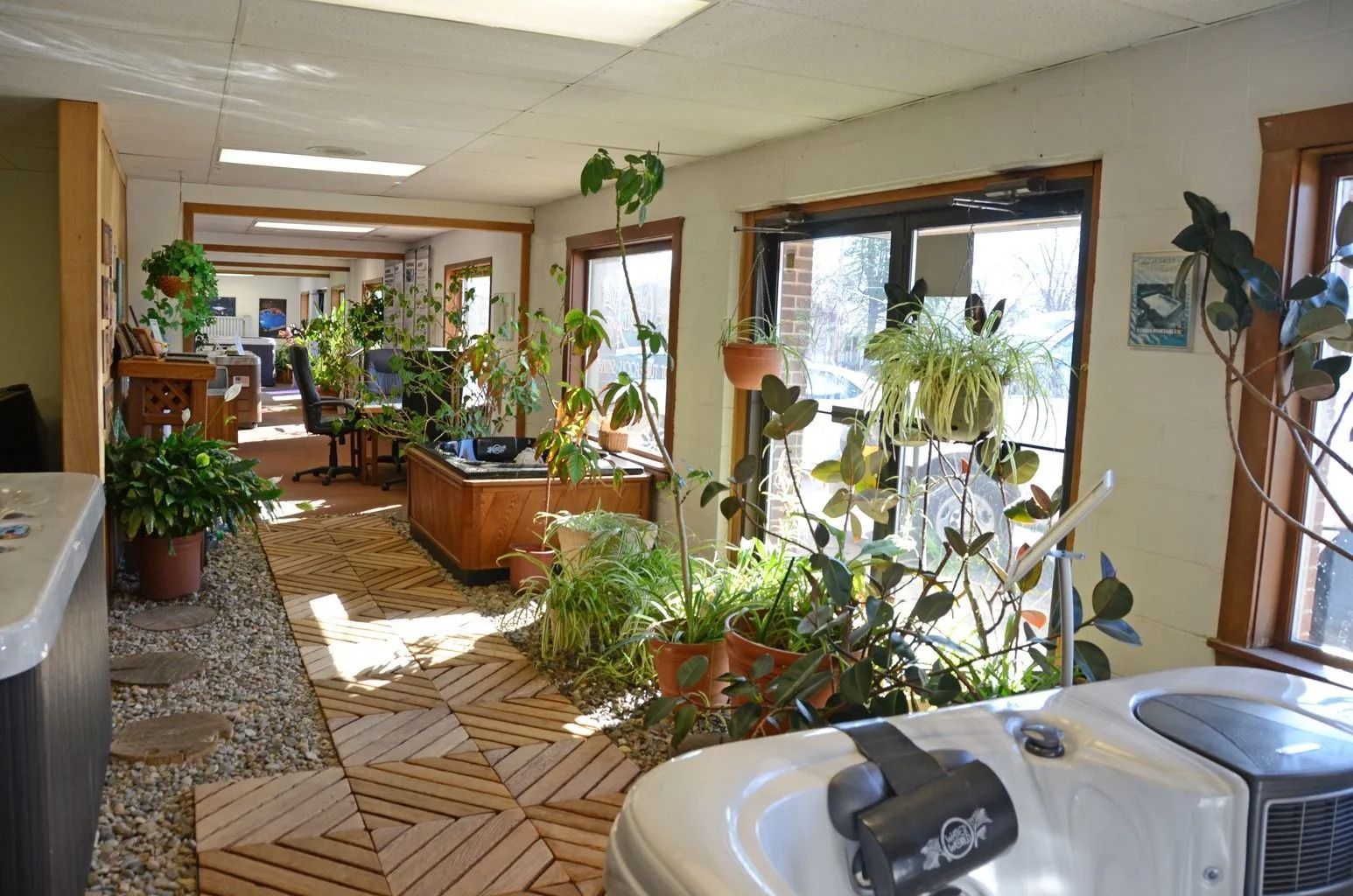 Indoor spa room with jacuzzi, plants, wooden floors, windows, and view into other rooms.