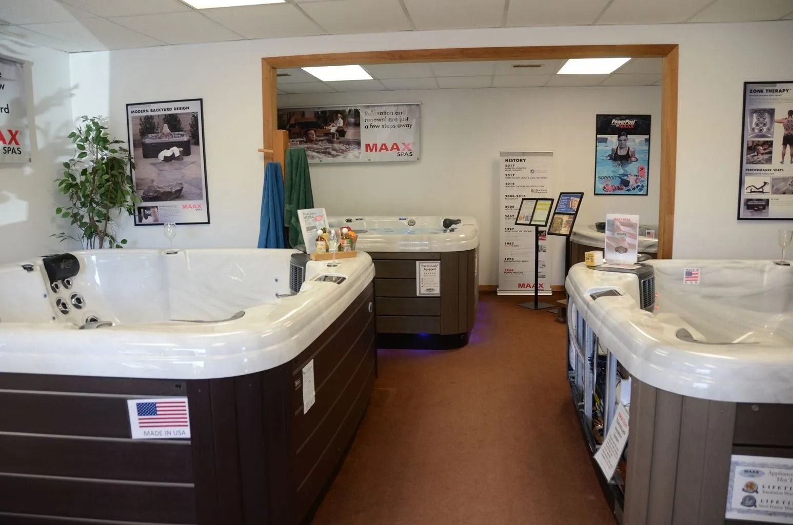 Hot tub showroom interior. Displays hot tubs, signs, and accessories on a brown floor.