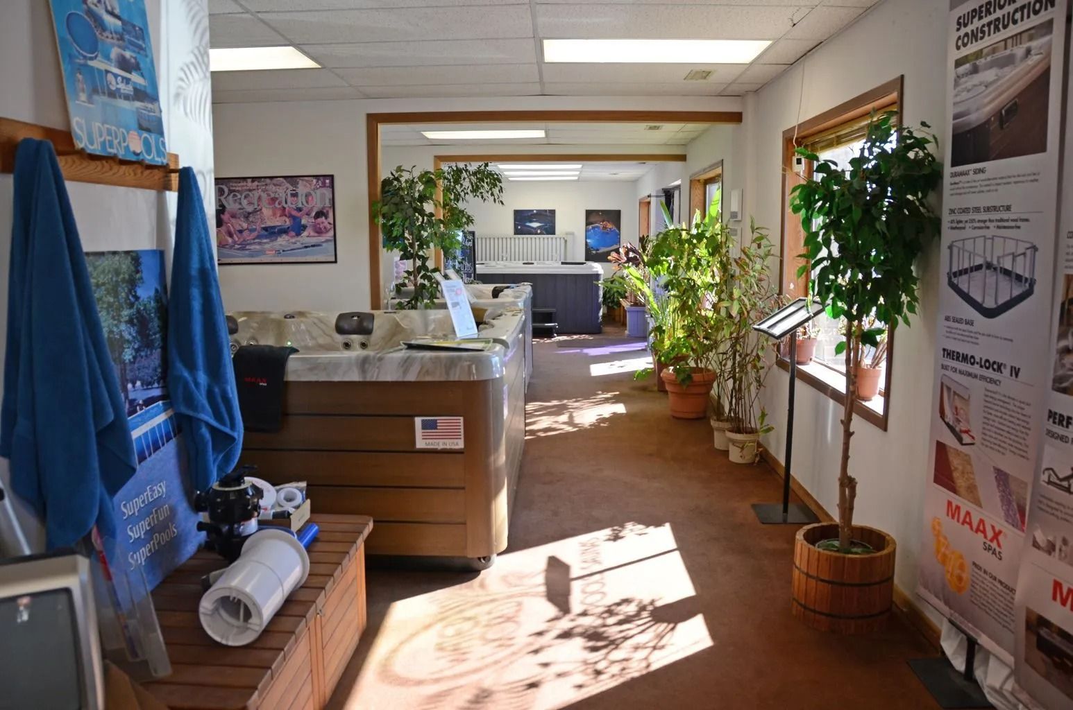 Hot tub showroom with tubs, plants, and product displays. Sunlight streams down the hallway.