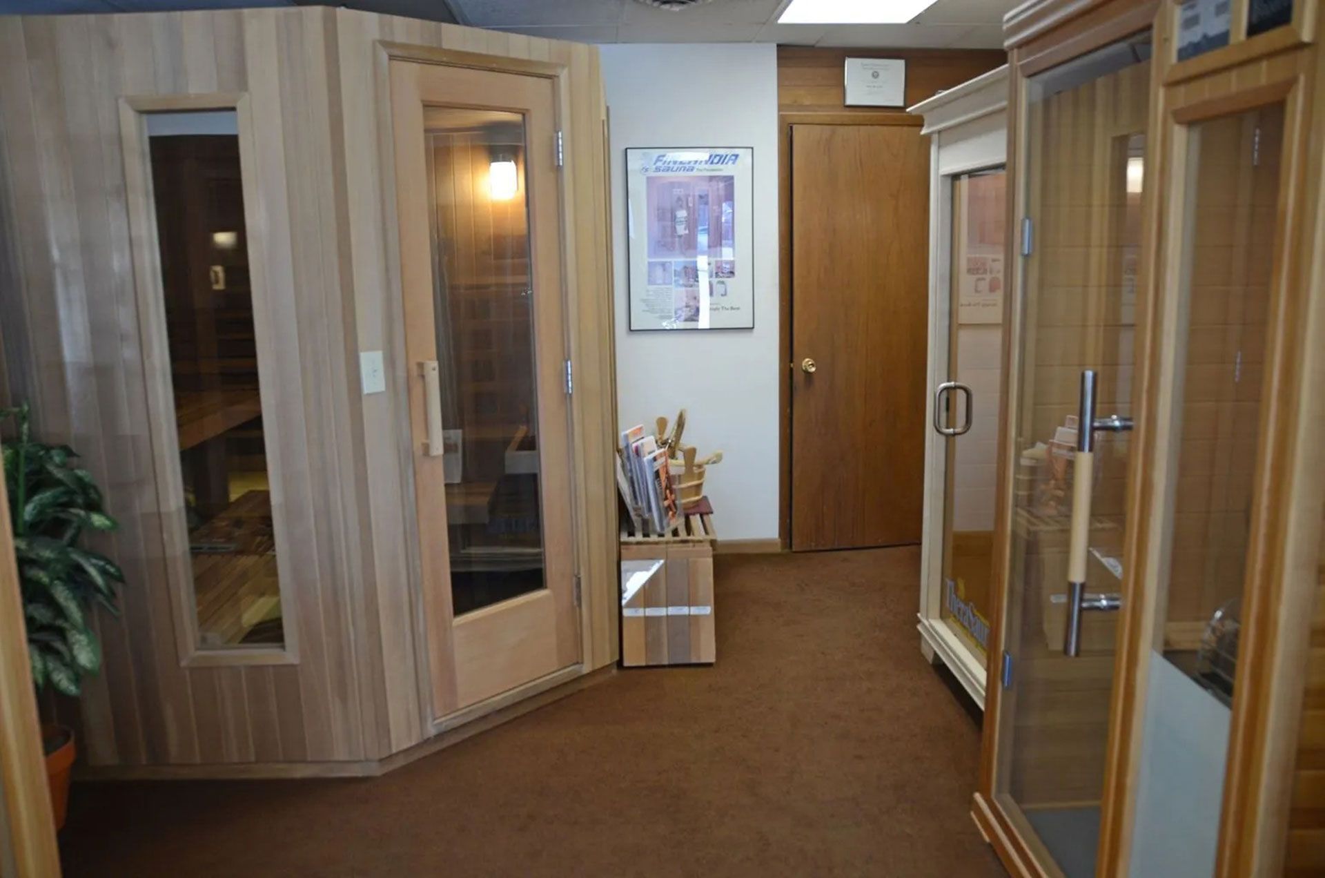 A showroom with saunas. Brown carpet, light wood saunas with glass doors, art on the wall.
