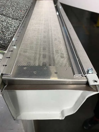 Gutter with attached metal mesh guard to prevent debris from entering the gutter system.