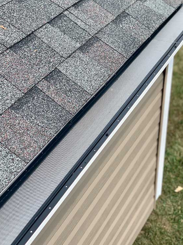 Close-up of a roof gutter with a mesh guard, installed on a building with brown siding.