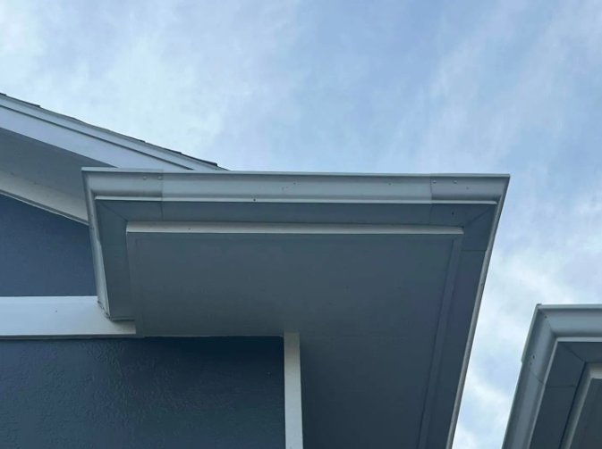 Gray roof edge and gutter against a cloudy sky.