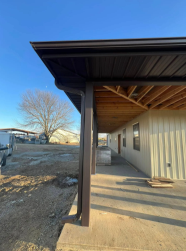 Brown roof overhang of a building, with a porch and metal siding in a rural outdoor setting.