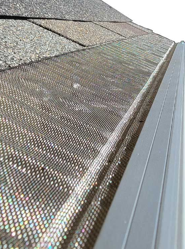 Close-up of a roof with shingled tiles and gutter guard screen, next to a silver rain gutter.