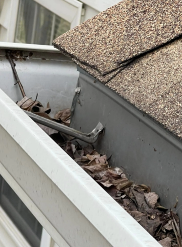 Gutter filled with leaves and a crowbar next to a roof.