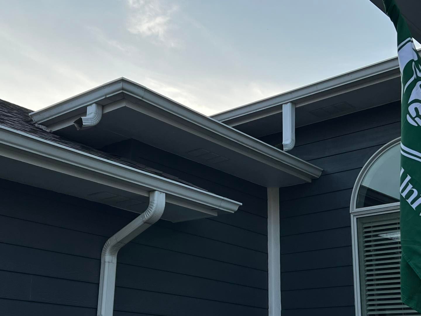 Grey house exterior with white gutters, downspouts, and a partly cloudy sky.