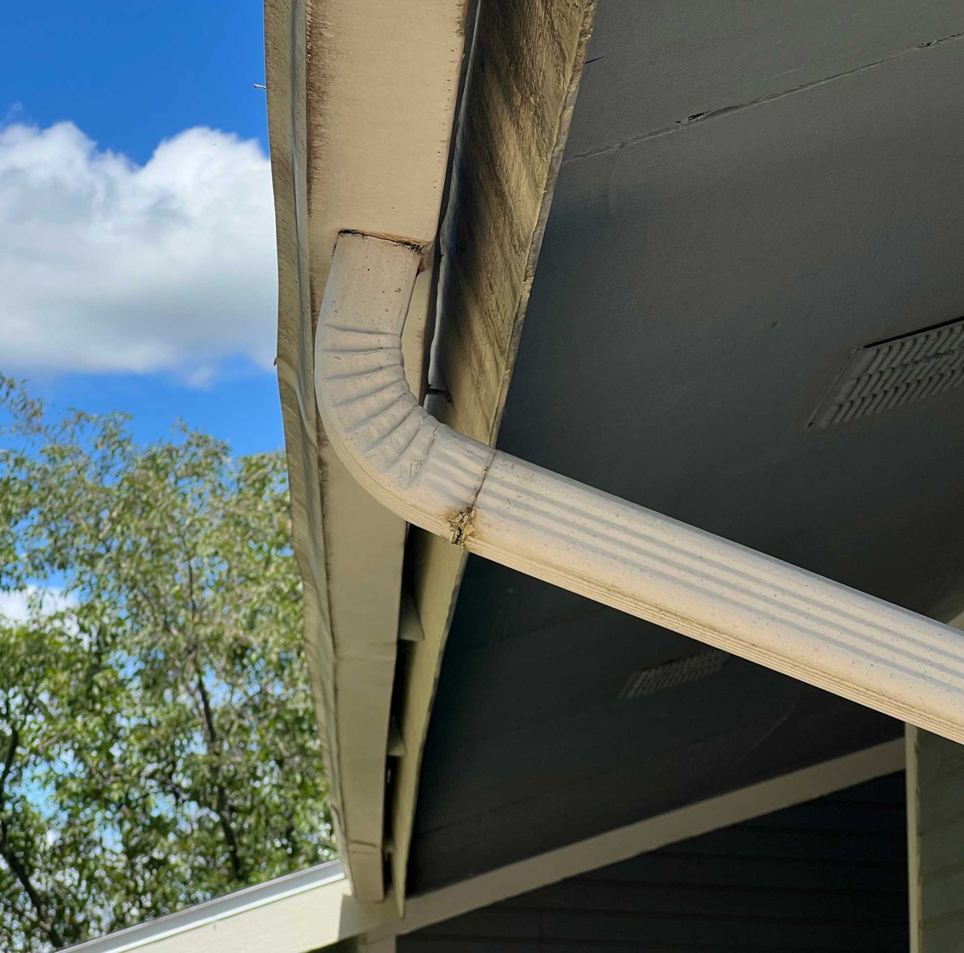 Close-up of white gutter and downspout on beige house
