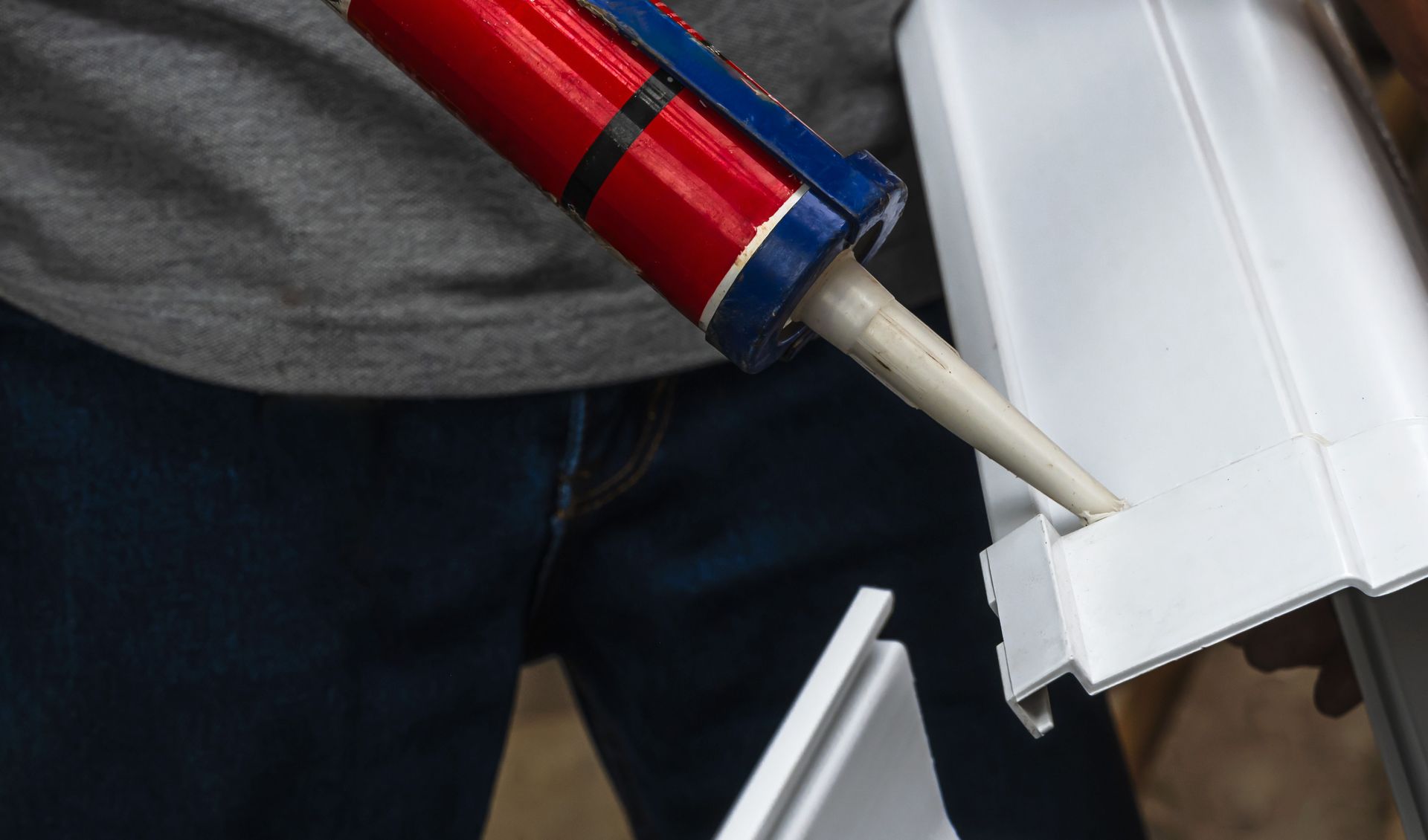Caulking gun applying sealant to a gutter