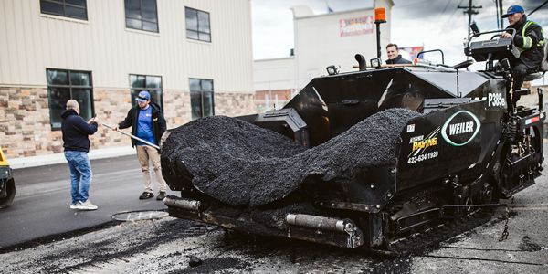 a man is standing next to a machine that is laying asphalt on a street