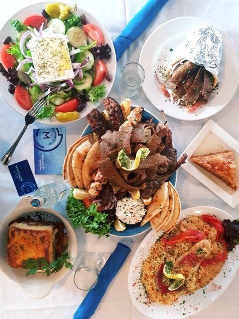A table topped with plates of food including a salad and gyros