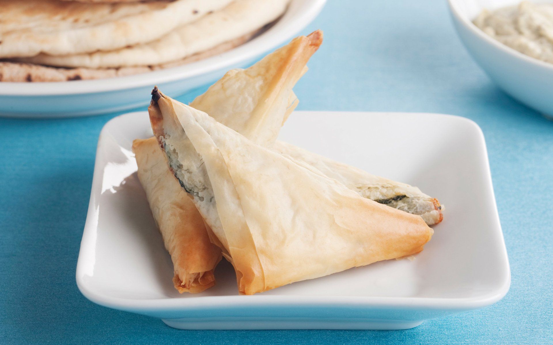 A white plate topped with three triangles of food on a blue table.