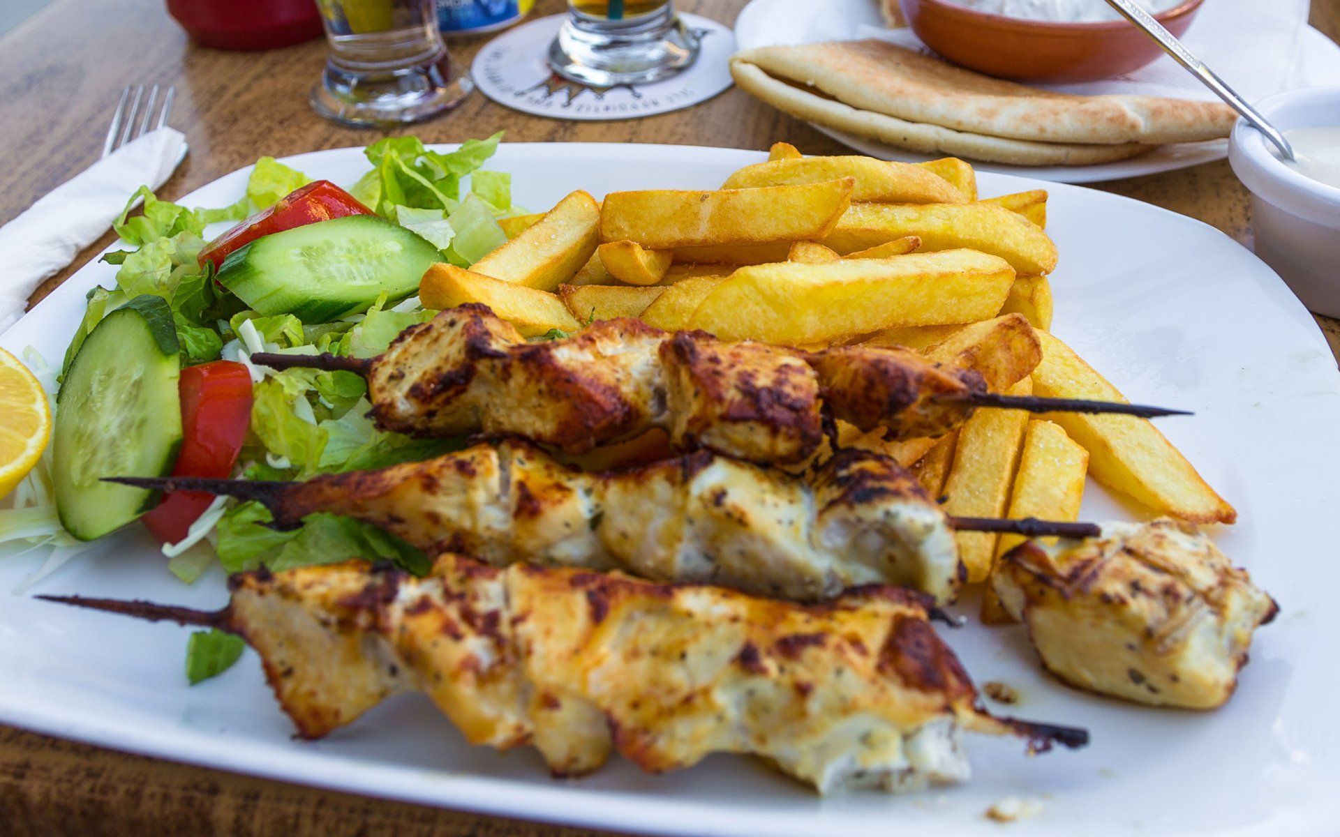 A white plate topped with chicken skewers and french fries.