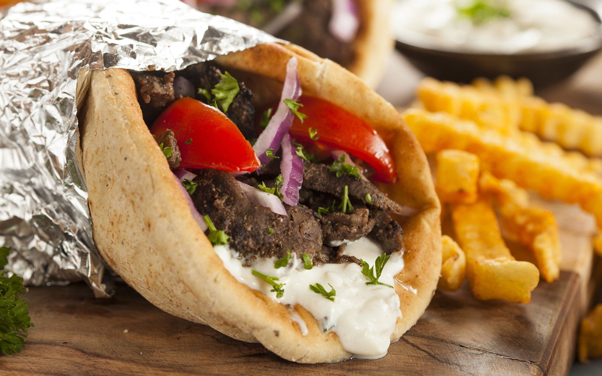 A close up of a gyro with french fries on a wooden table.