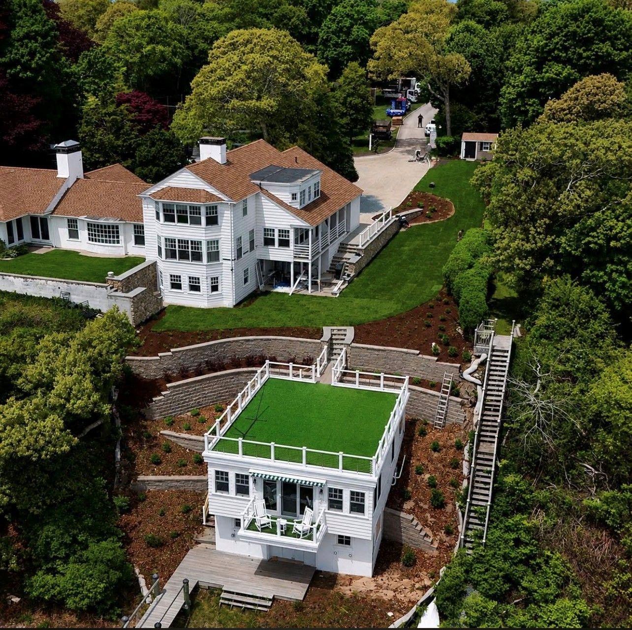 Aerial view of a white house with red roof and green rooftop terrace amid lush trees and landscaped slopes