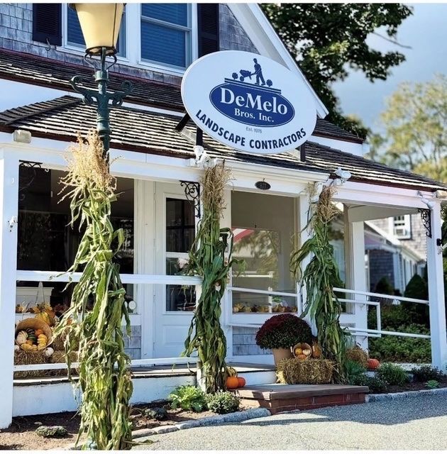 DeMelo Landscape Contractors storefront with white porch, hanging plants, and garden displays
