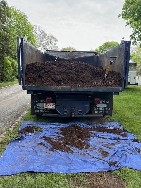 Dump truck unloading dirt onto a blue tarp along a roadside