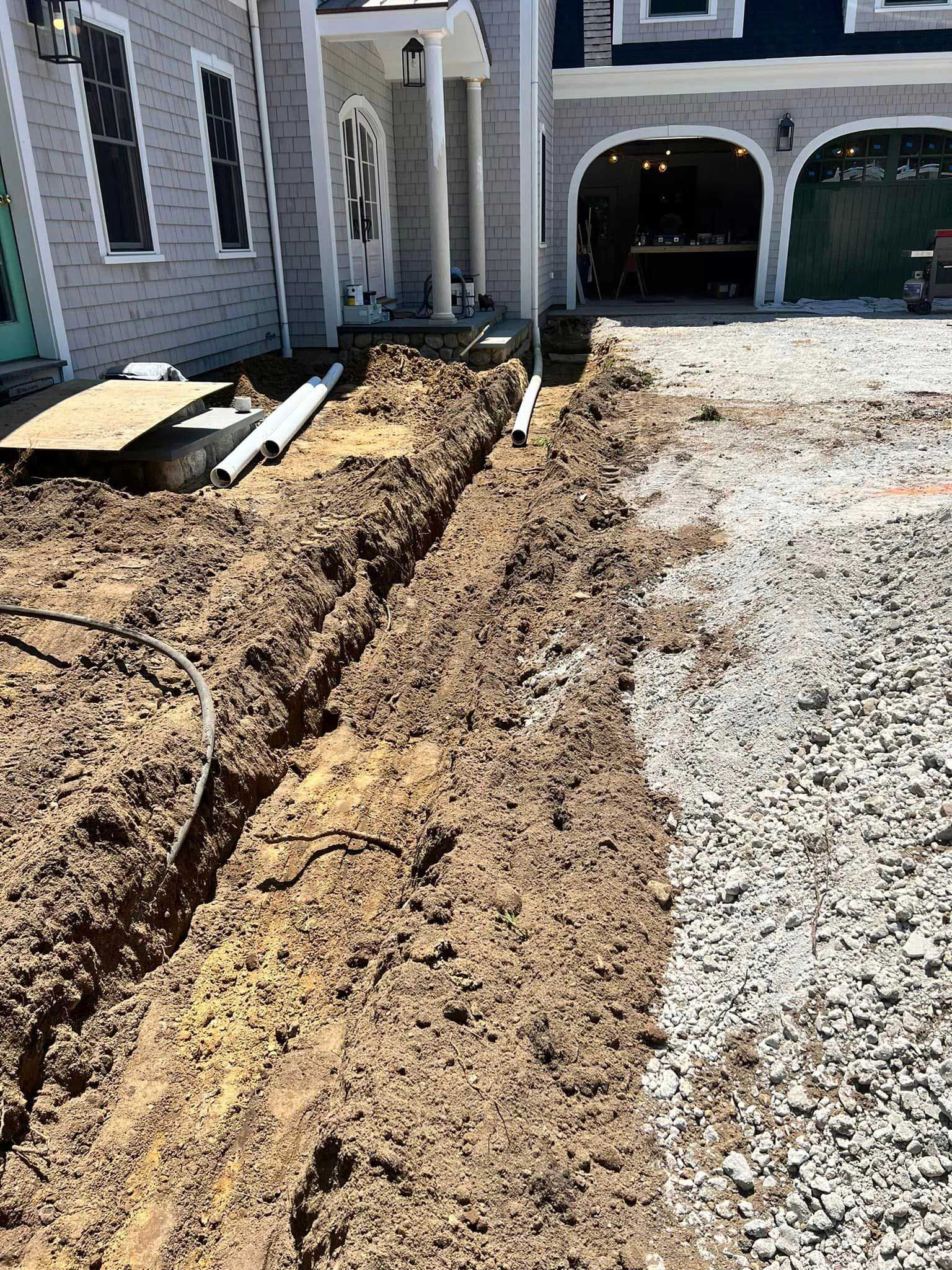 Freshly dug trench along a gravel driveway beside a house under construction