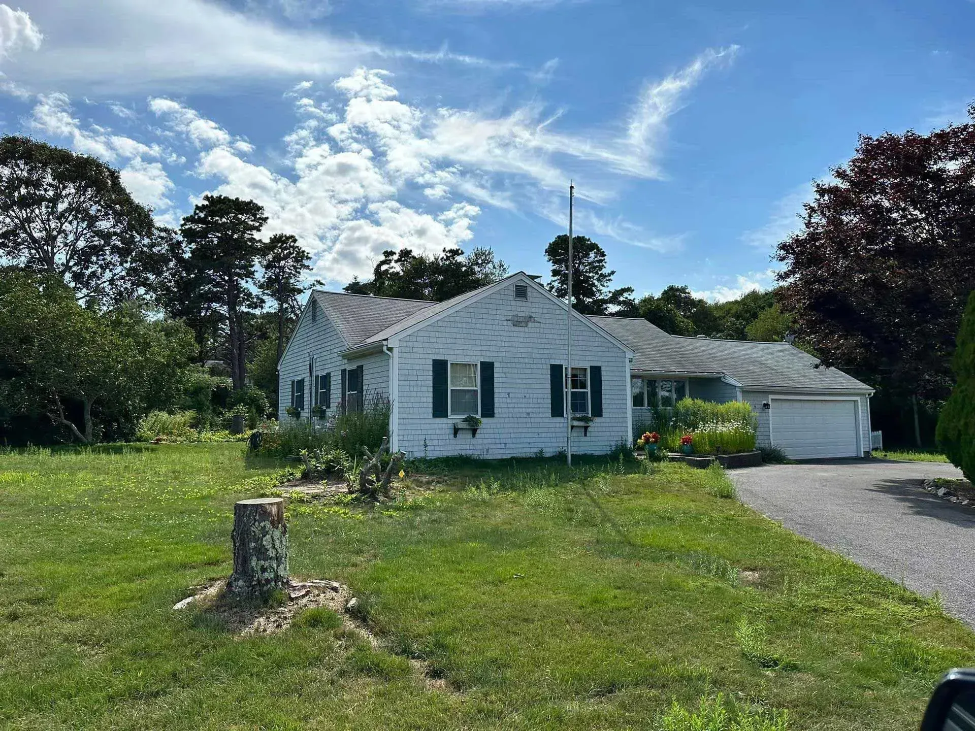 White house with green shutters and attached garage on a grassy lot under a blue sky