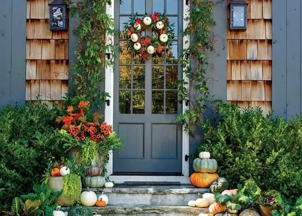 Gray front door with autumn wreath, pumpkins, and colorful potted flowers by a stone step