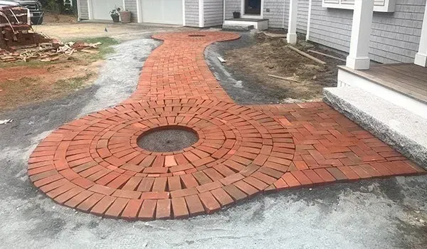 Curved brick walkway around a circular drain, leading between two houses