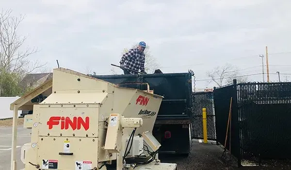 Worker standing on a FINN wood chipper beside a black truck in an outdoor yard