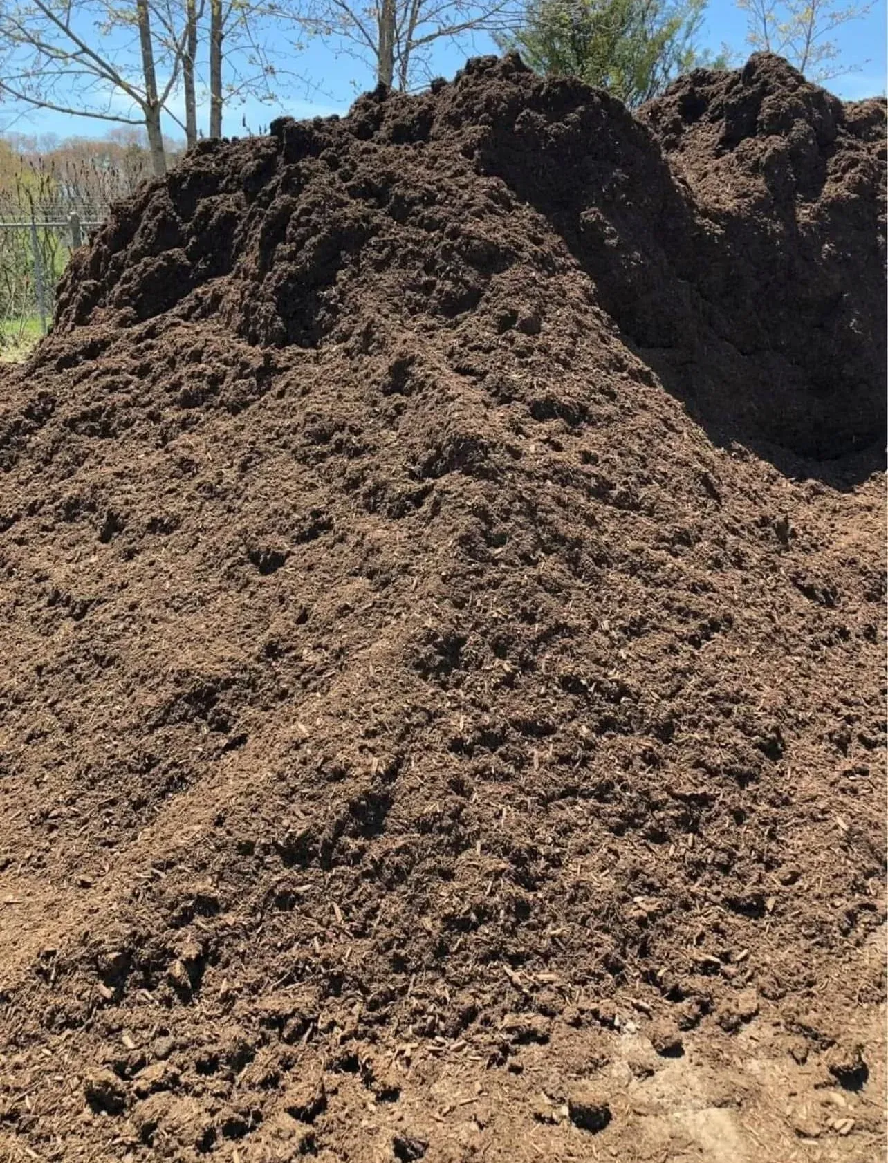 Large pile of brown dirt or mulch outdoors under a clear blue sky.