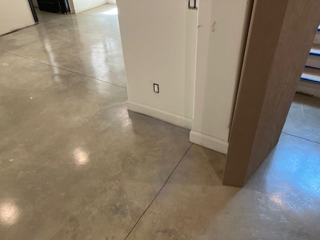 Polished concrete floor in a hallway with white walls, baseboard and an electrical outlet. Cardboard leaning against the wall.