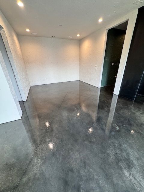Empty room with polished concrete floor, white walls, recessed lighting, and a dark doorway.