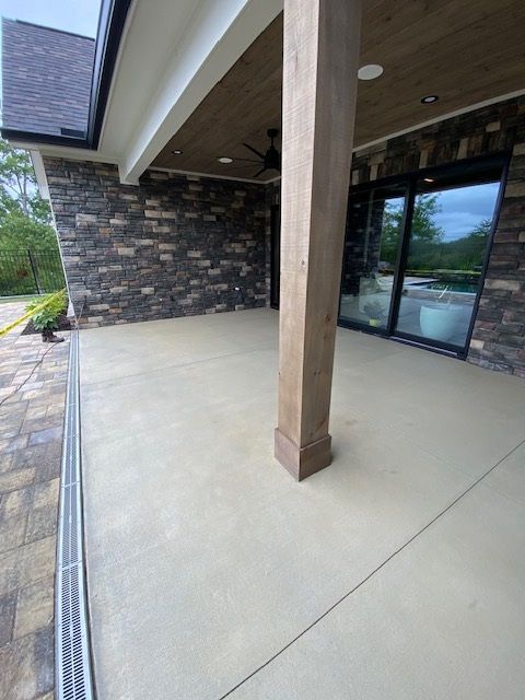 Concrete patio with stone wall, wooden beams, sliding glass door, and a drainage system.