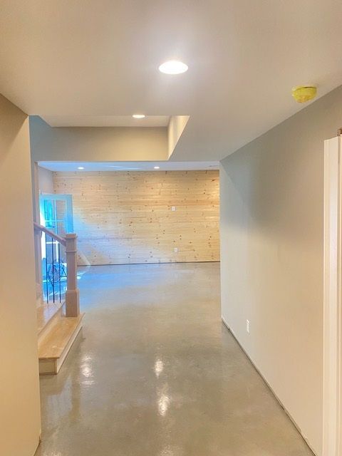 Hallway with concrete floor leading to an unfinished room with wooden wall.