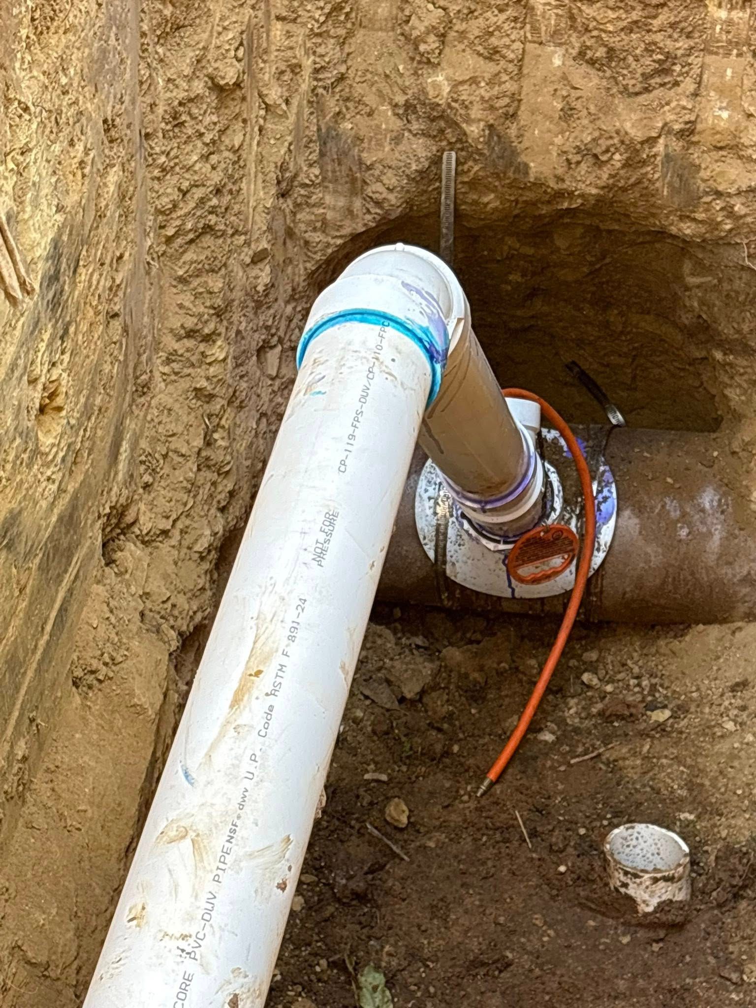 PVC pipe connected to a larger brown pipe in a dirt trench, with wiring visible.