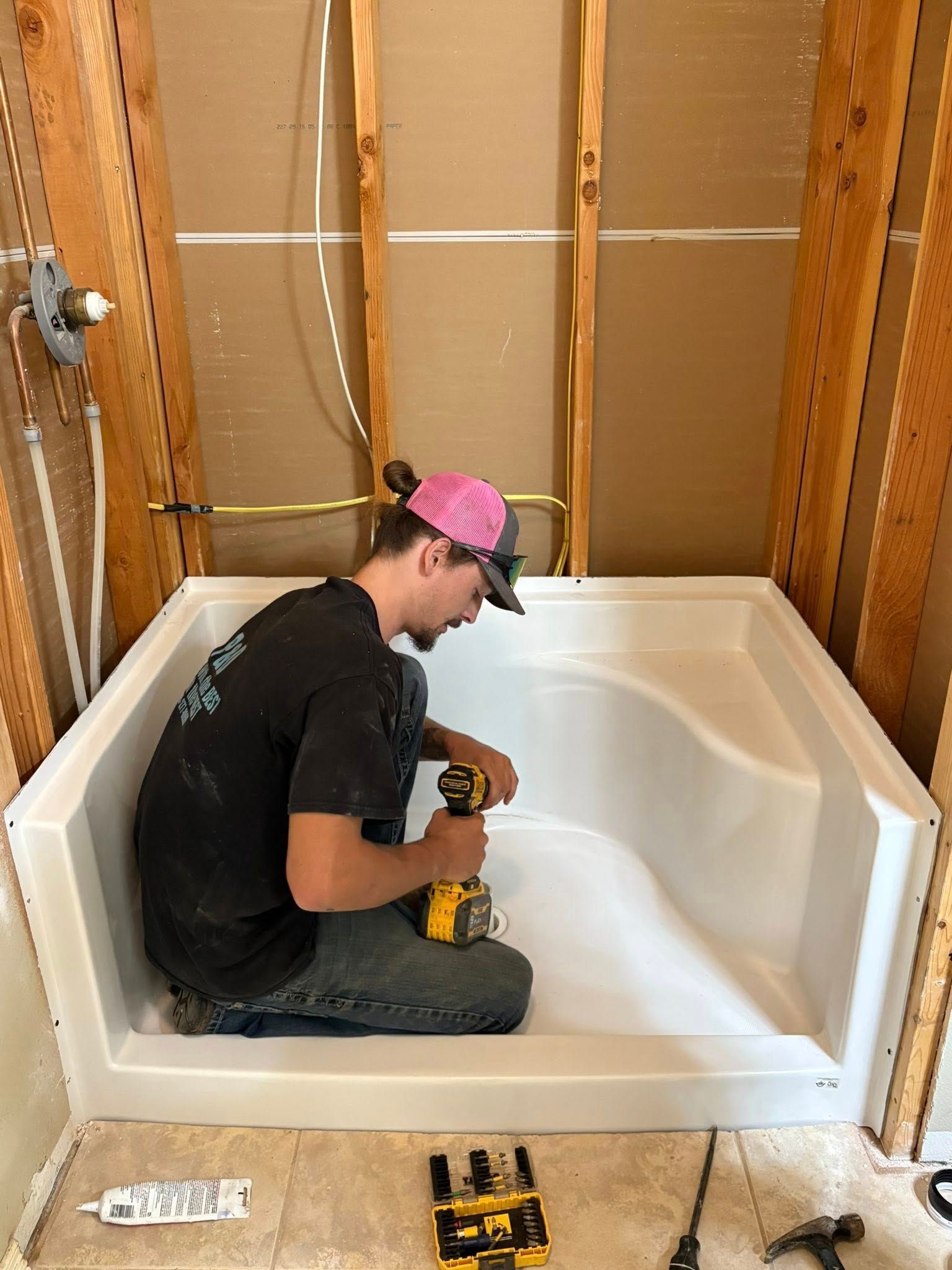 A person installing a white shower base in a bathroom under construction, using a drill.