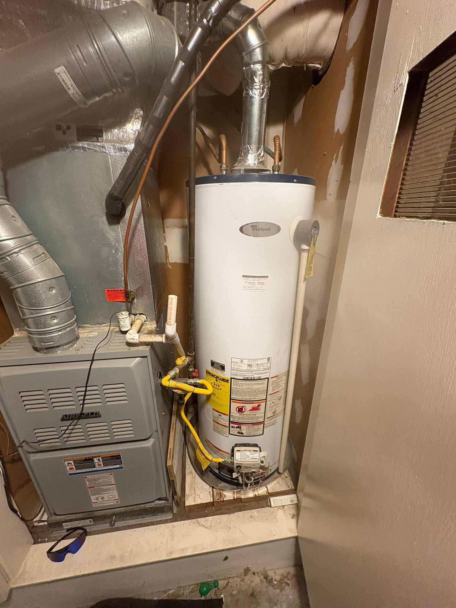 Furnace and water heater in a utility closet with vent pipes, electrical wiring, and plumbing.