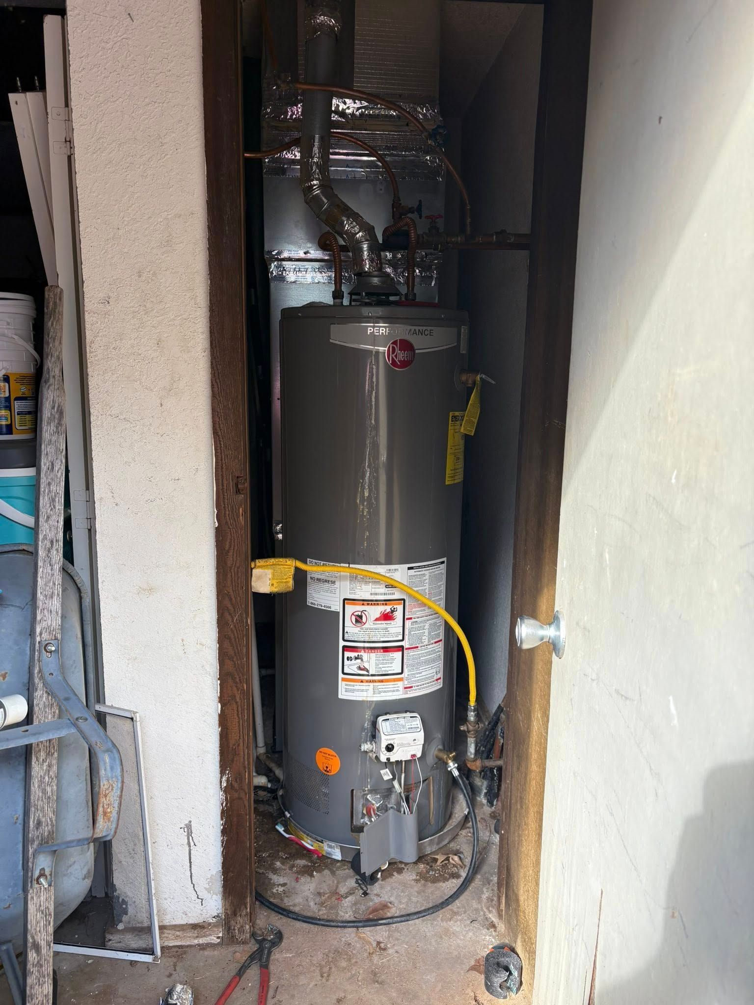 Water heater in a narrow closet with metal vent, gas line, and electrical cord.
