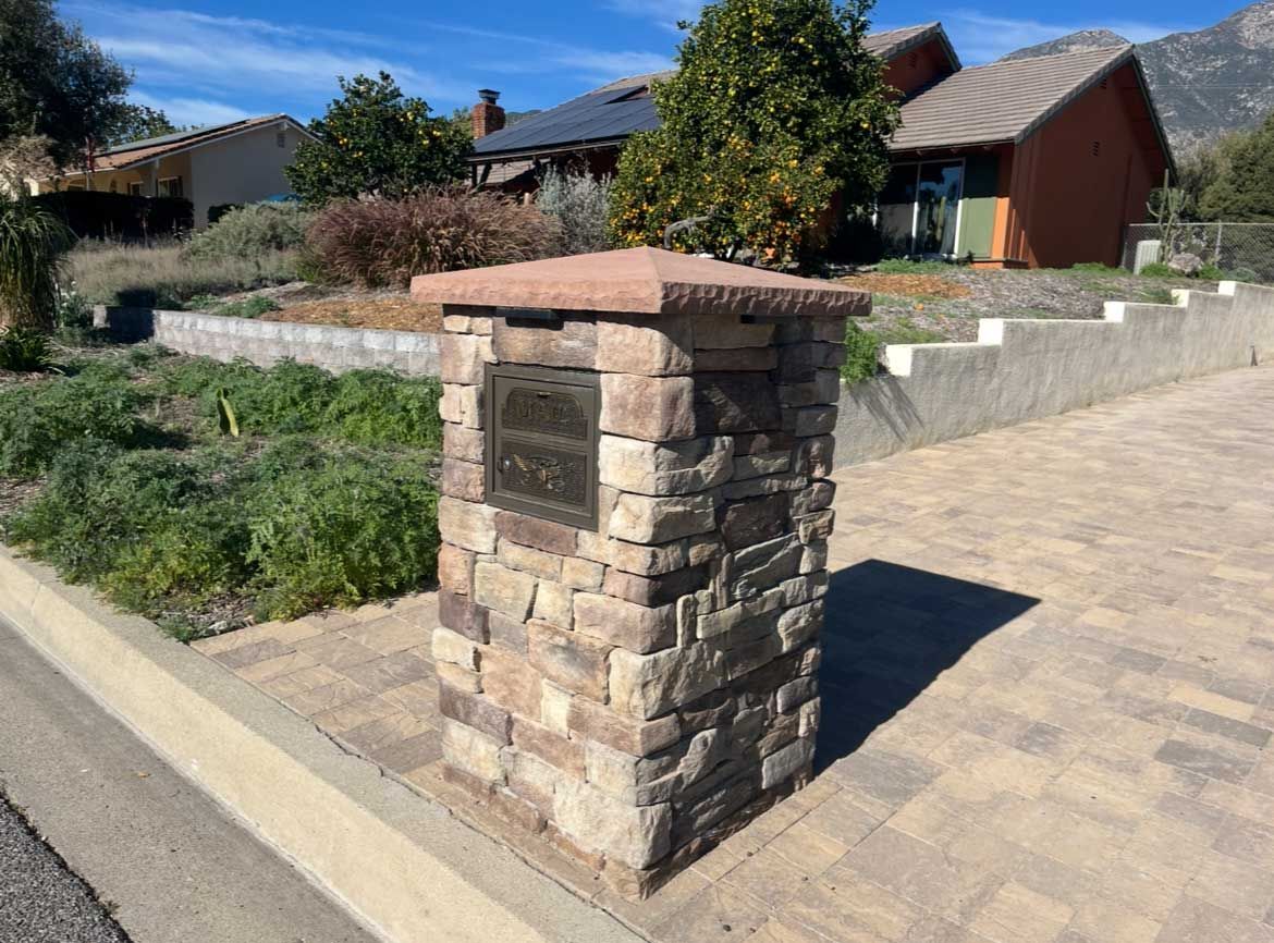 Stone pillar with bronze plaque on a brick-paved sidewalk in front of houses.