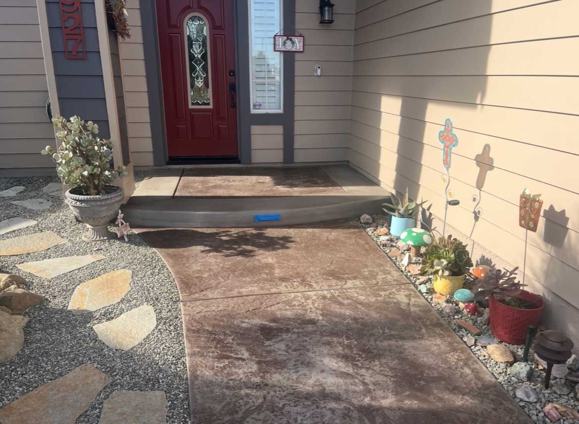 Entrance to a house: red door, concrete steps, walkway, potted plants, gravel, and stone path.