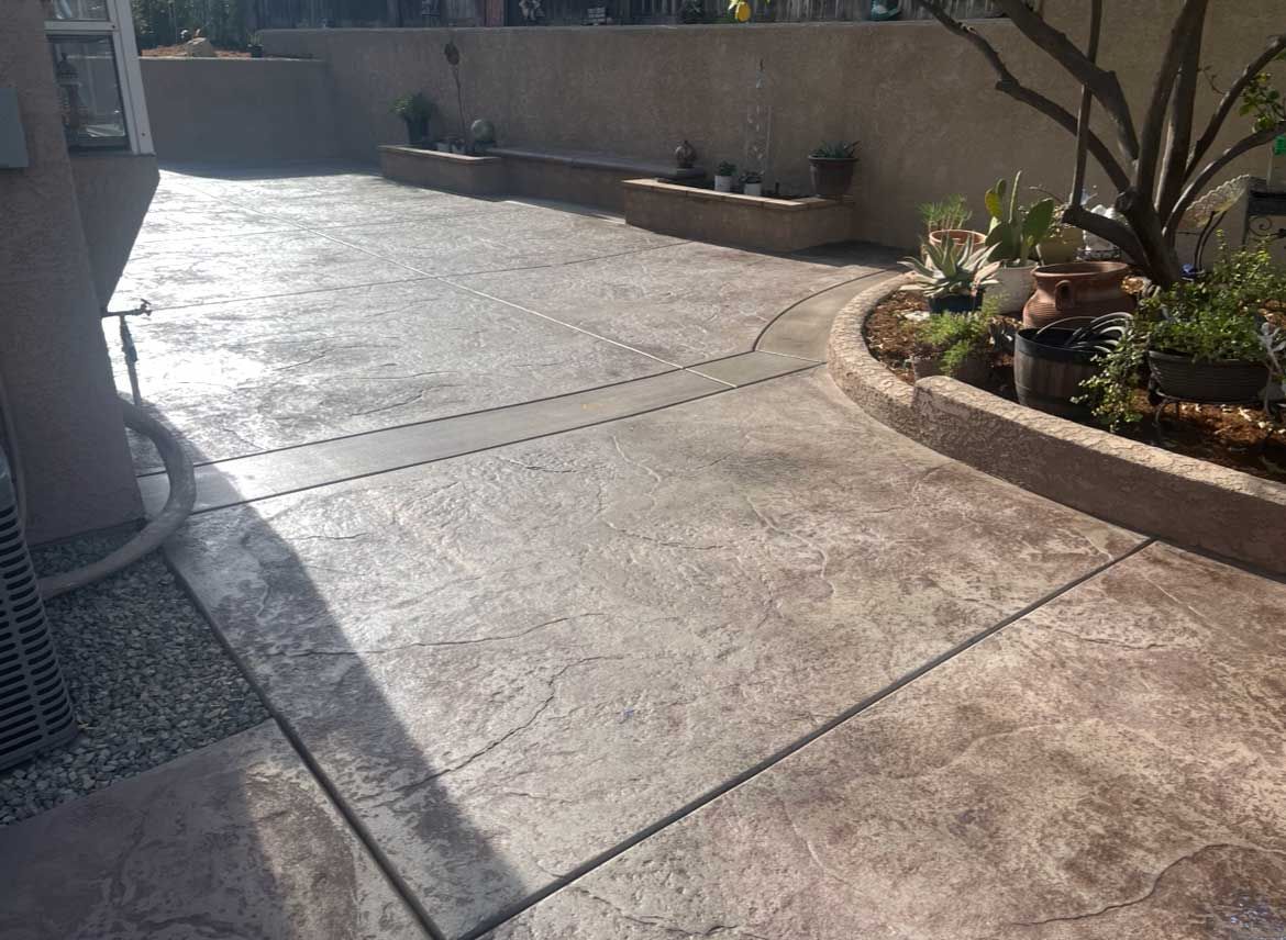 Concrete patio with textured surface, planter, and small tree. Brown and gray tones.