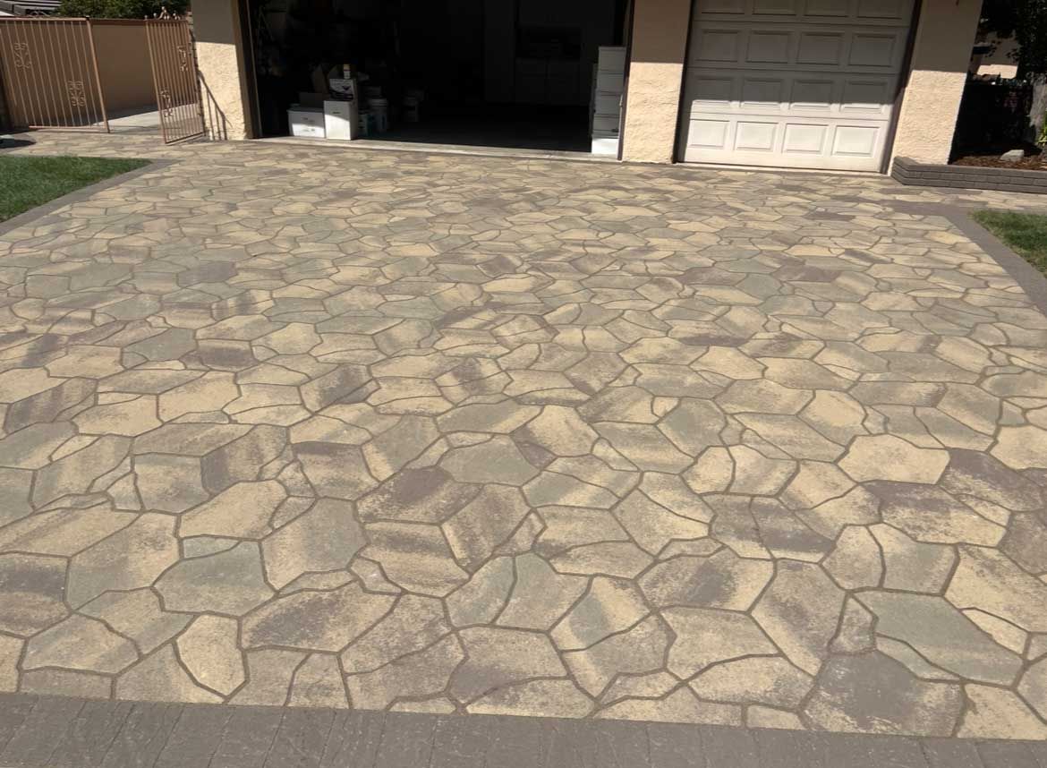 Driveway paved with tan and grey patterned stones in front of a garage.