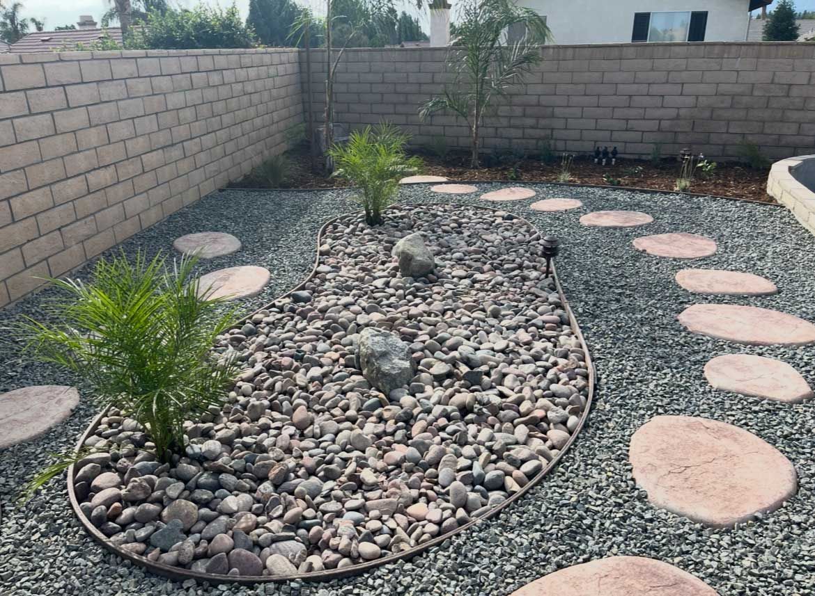 Backyard with stone path, rock bed, plants, and brick wall.
