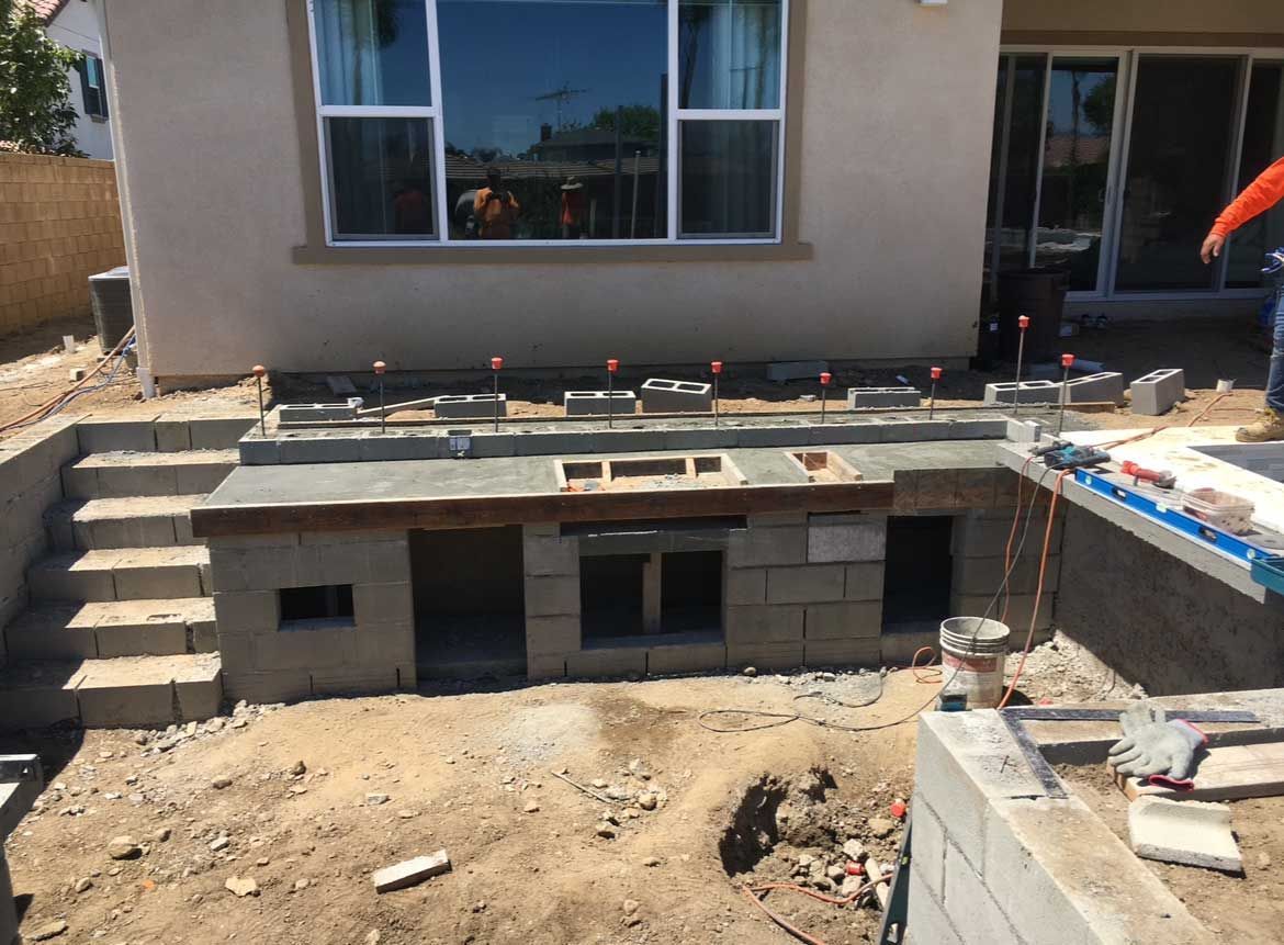 Outdoor kitchen under construction, built from cinder blocks, with stairs and windows visible.