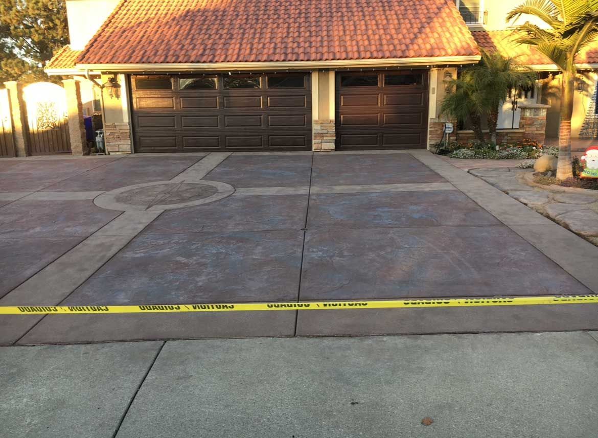 Driveway with dark garage doors, decorative concrete design, and caution tape.