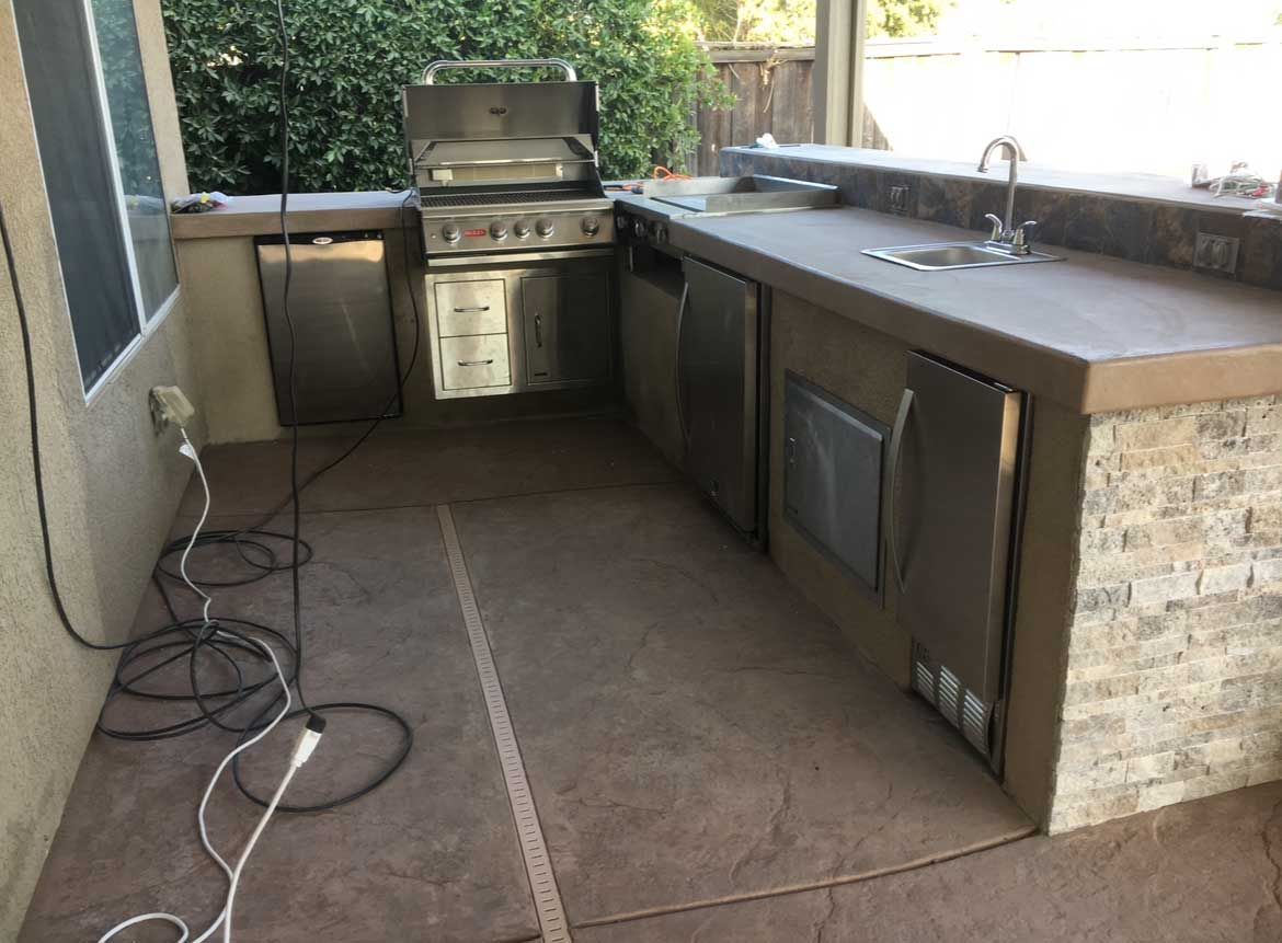 Outdoor kitchen with grill, sink, and built-in appliances on a concrete patio.