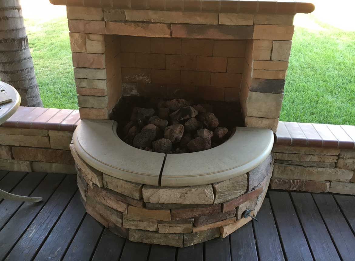 Stone fireplace built into a deck, filled with wood.