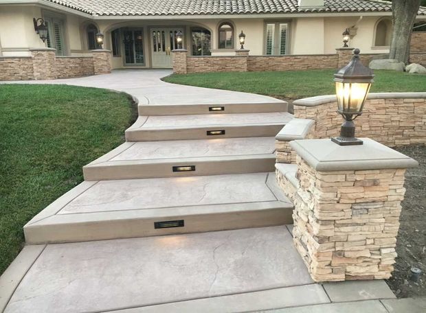 Stone steps with built-in lights lead to a house with a stone facade, alongside a pillar with a lamp.