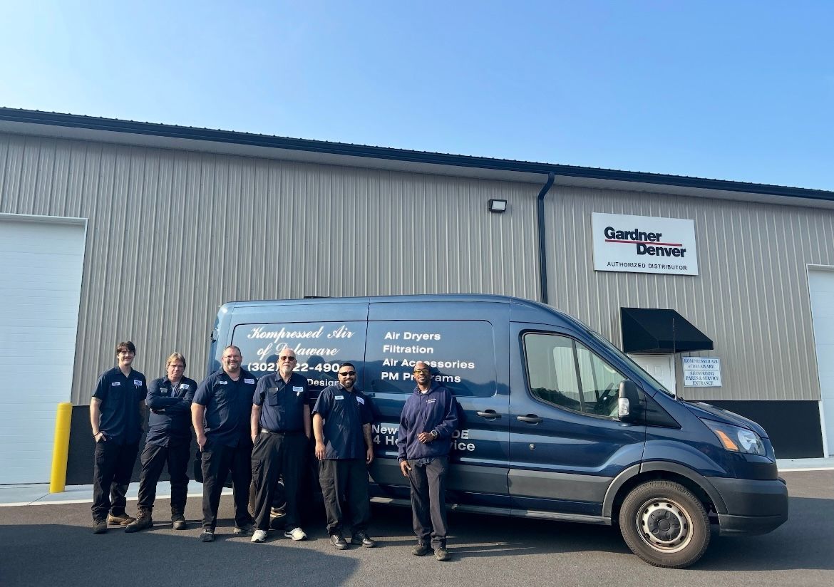 A team of HVAC technicians standing next to their service van in front of a building.