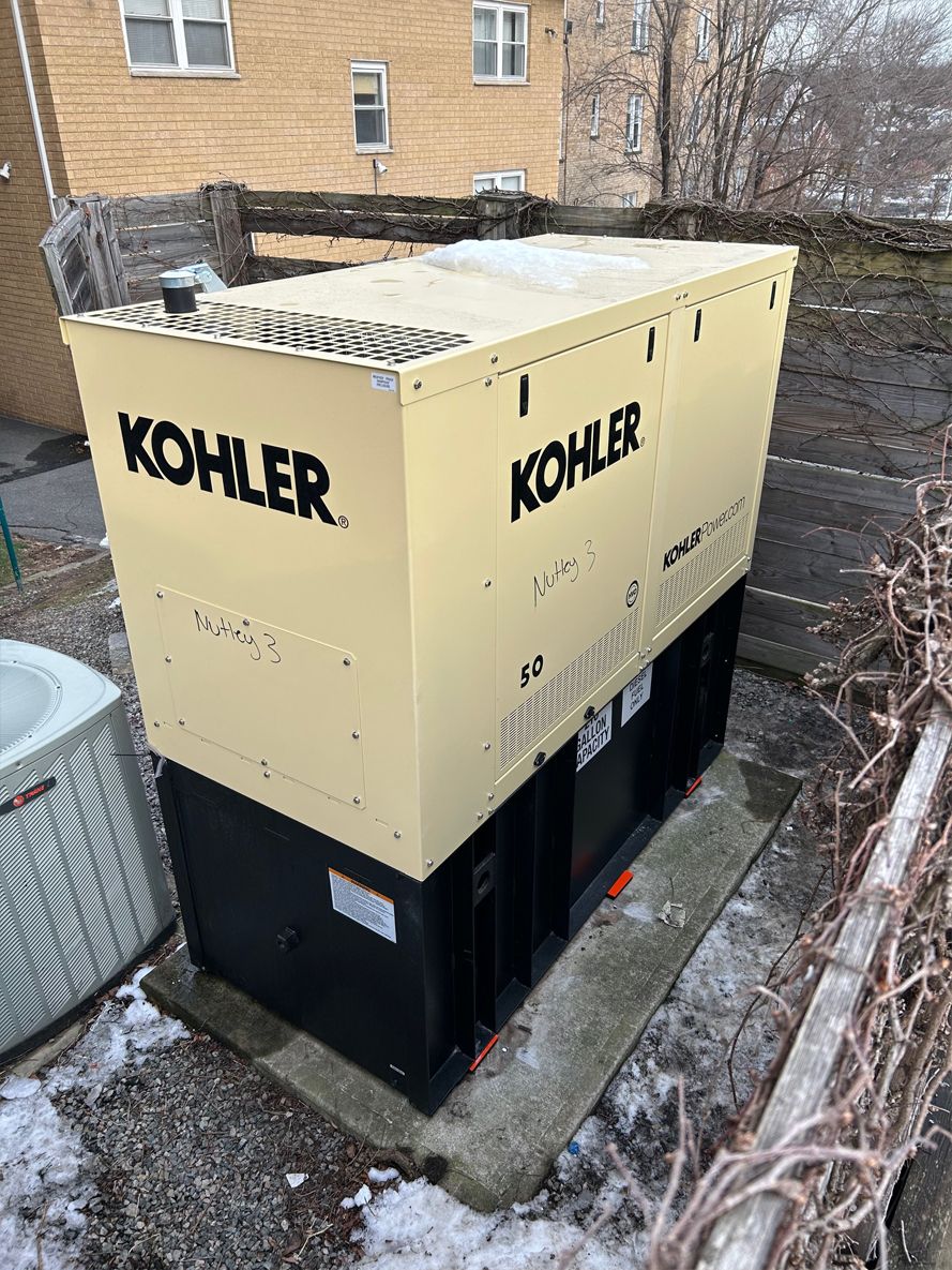 A kohler generator is sitting in the snow in front of a brick building