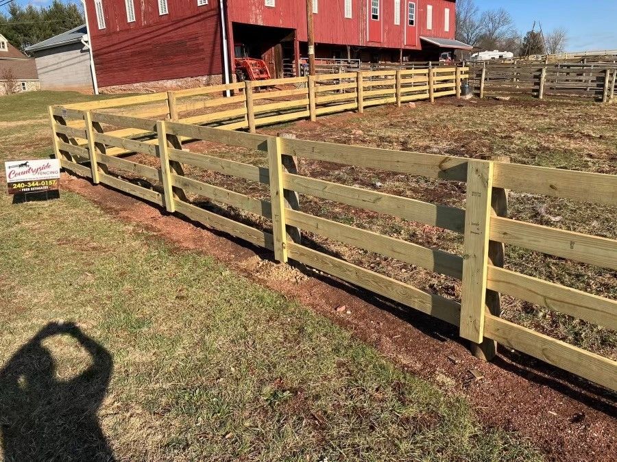 A wooden fence in a field with a red barn in the background.